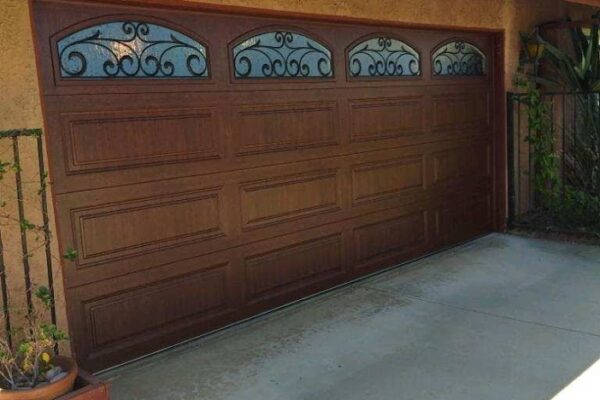 Premium Series walnut-finish garage door with recessed panels and arched windows featuring decorative wrought iron grilles.