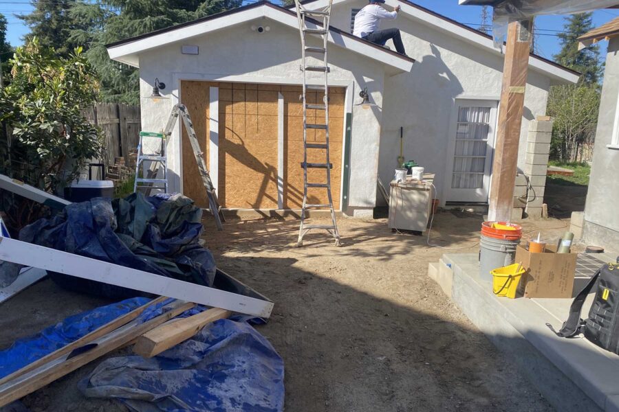 Construction site showing a garage renovation with a worker on the roof and a boarded-up garage door opening.