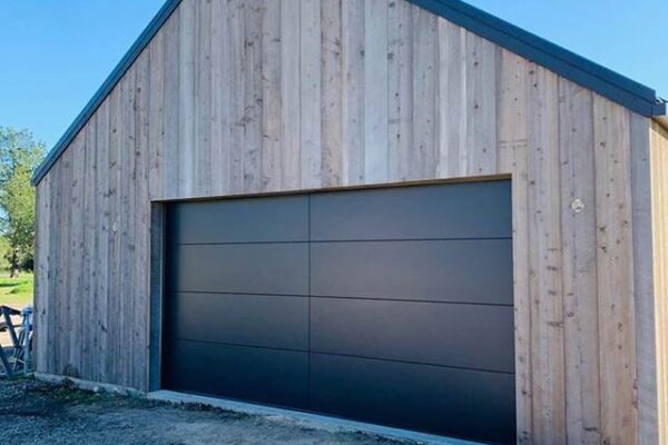 Modern black garage door installed on a wood-sided barn style building in Redlands, CA.