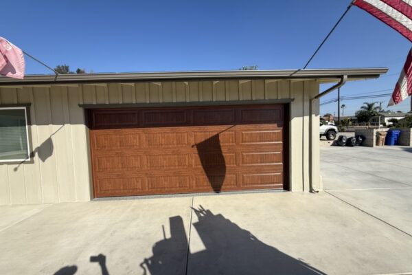 Brown wood-look garage door installed on a detached garage with beige siding and concrete driveway