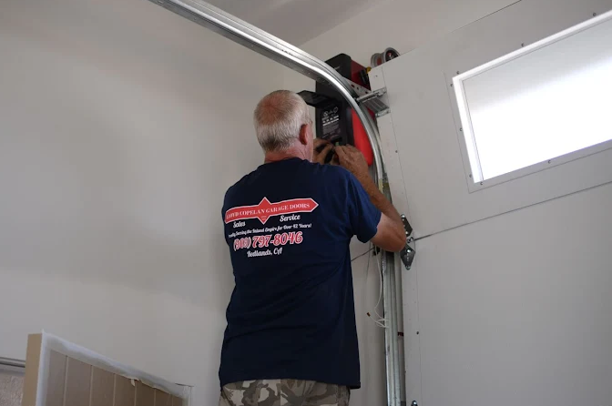 Lloyd Copelan Garage Doors technician installing a garage door opener inside a home garage in Redlands, CA.