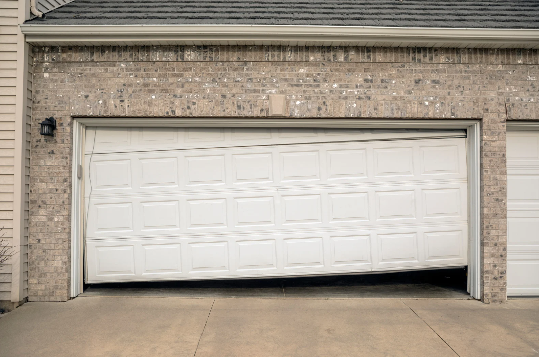 White residential garage door bent and off track at a home in Redlands, CA requiring repair.