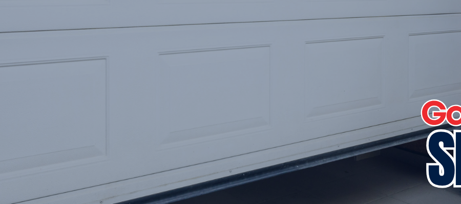 A wide panoramic white panel garage door installed on a residential home with stone accents, showcasing professional garage door services.
