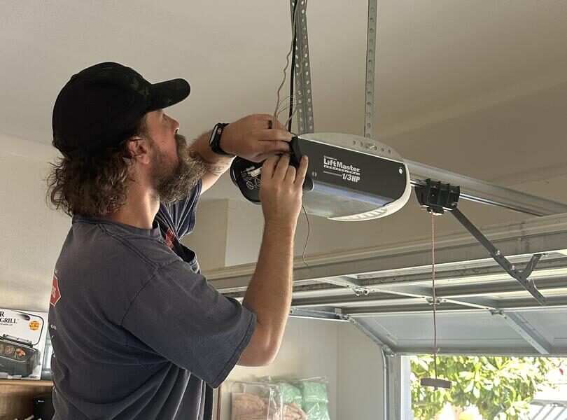 Technician JC from Lloyd Copelan Garage Doors inspecting and servicing a LiftMaster smart garage door opener attached to the ceiling.
