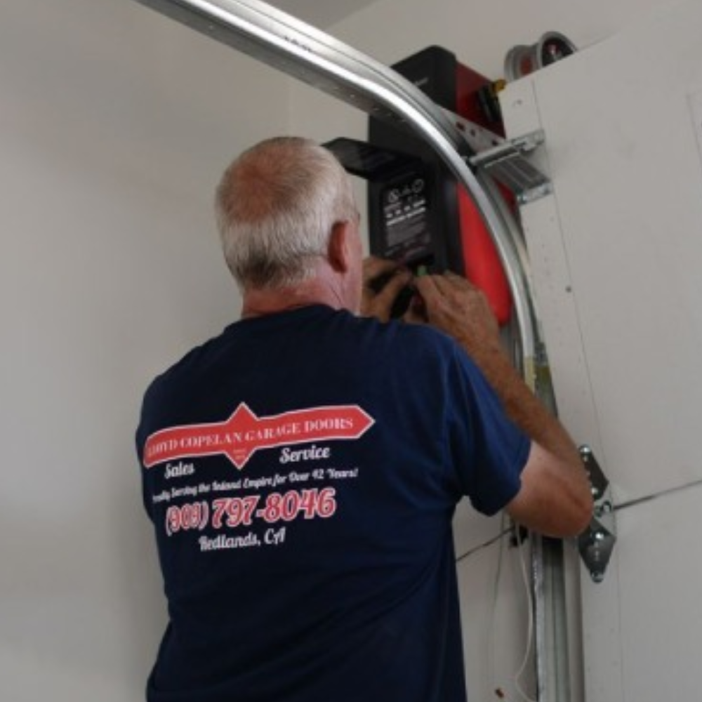 Lloyd Copelan technician performing maintenance beside a garage door track and opener
