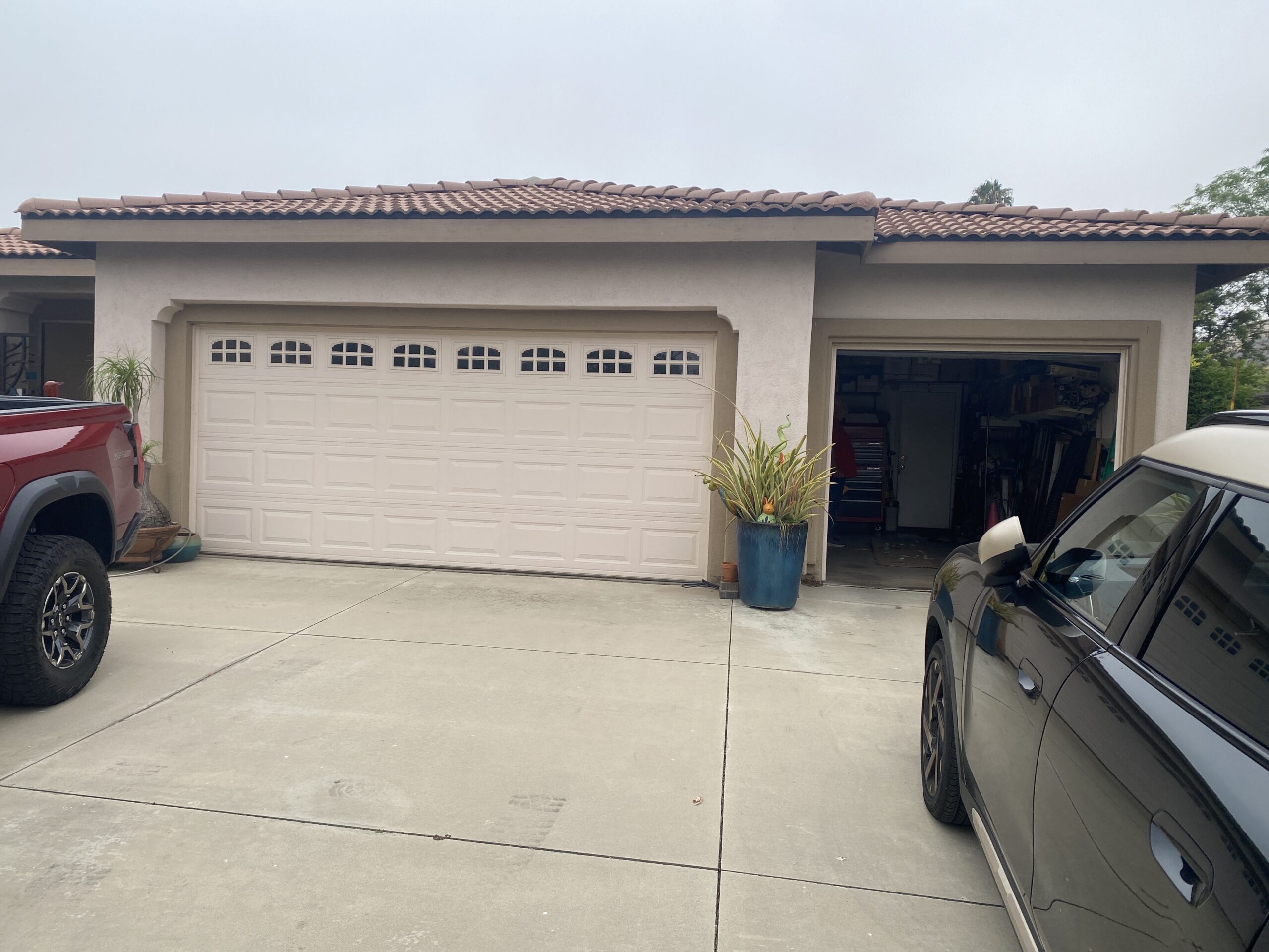 Before: A light-colored paneled garage door with arched windows beside an open garage bay at a Loma Linda home.