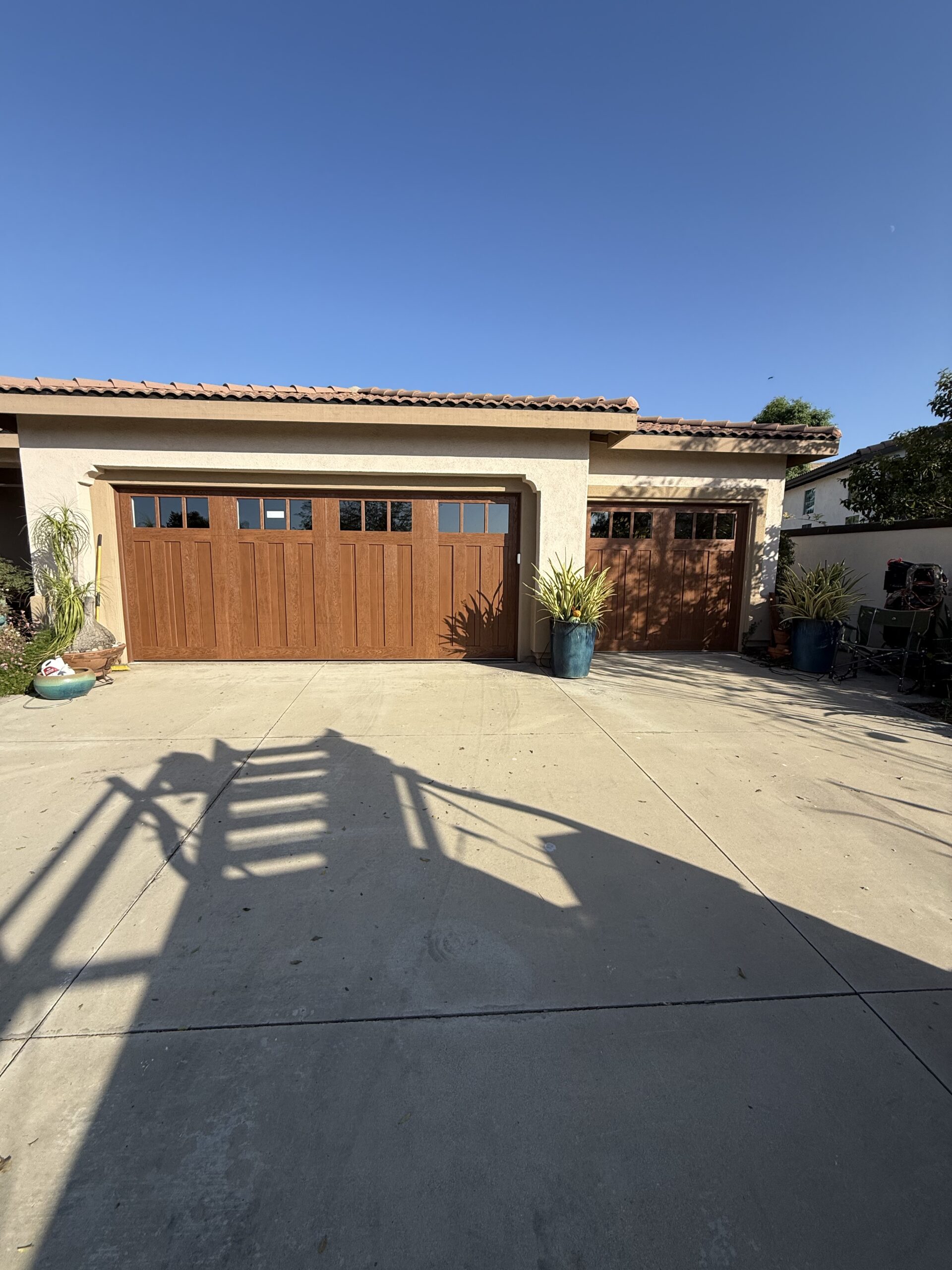 After: Two five-layer Clopay Canyon Ridge garage doors in a warm wood-look finish with top-section windows at a Loma Linda home.